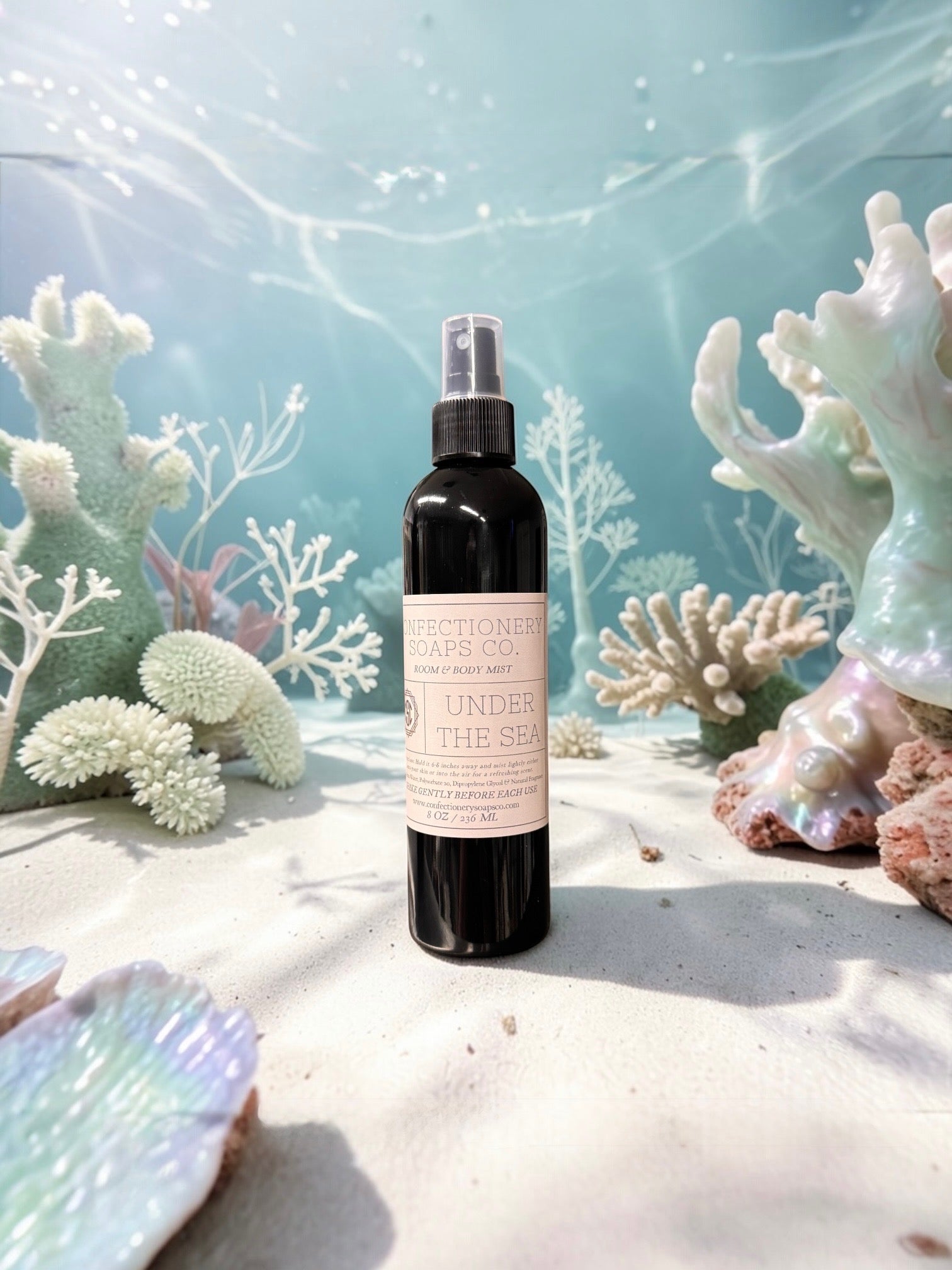 Black spray bottle with a label on a sandy beach with coral and sea shells in the background