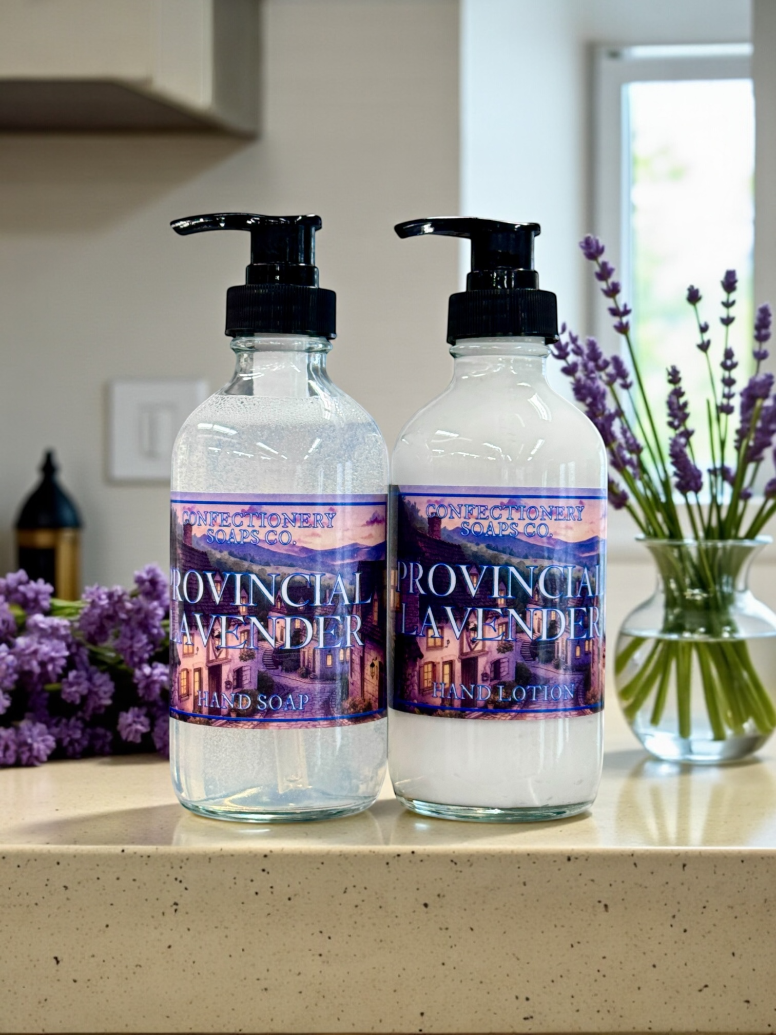 Glass bottle of hand lotion setting next to a glass botte of liquid soap with black pumps on a countertop with a bouqet of lavender in a vase