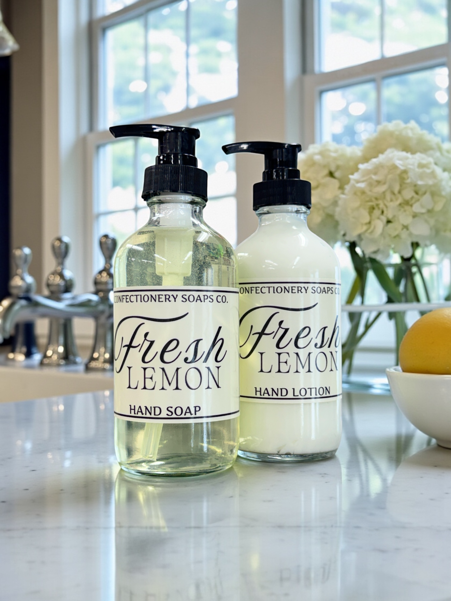 Two bottles of Fresh Lemon hand soap and lotion on a countertop with flowers in the background.