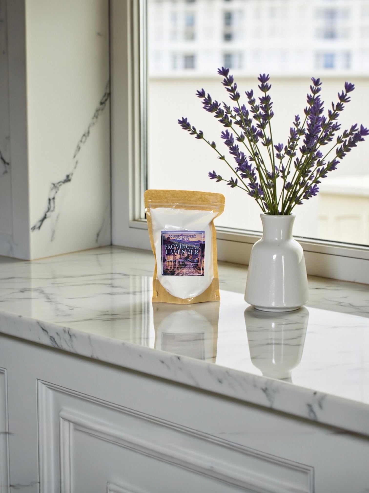 Lavender product packaging on a marble countertop with a vase of lavender flowers.
