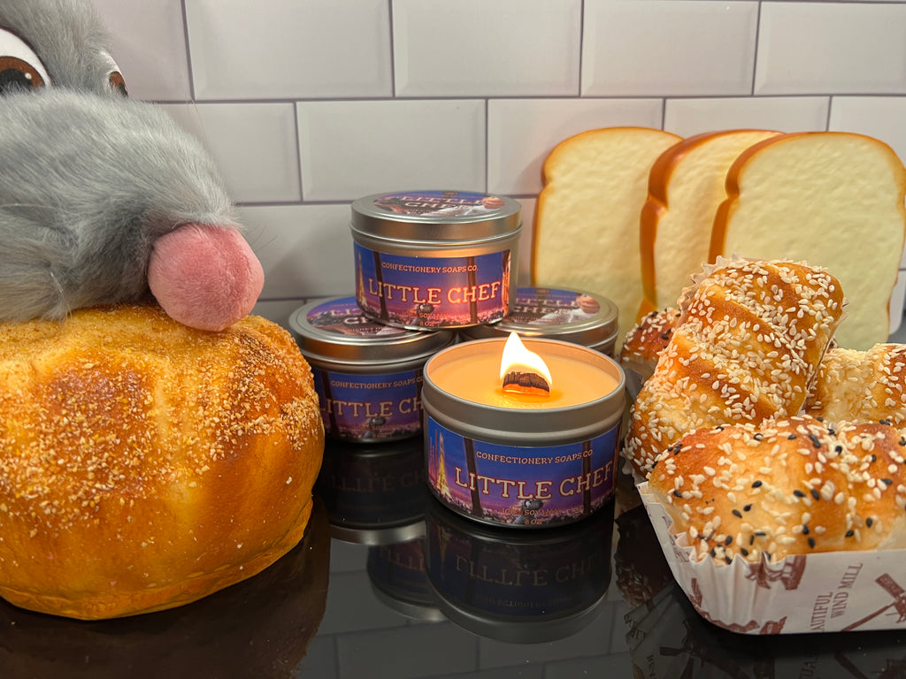 three little chef candles stacked in a triangular arrangement. in front of stack is a lit little chef candle. to the right of the candles are multiple pieces of fake bread as decor. to the left of the candles is a Remi from ratatouille puppet on a fake loaf of bread