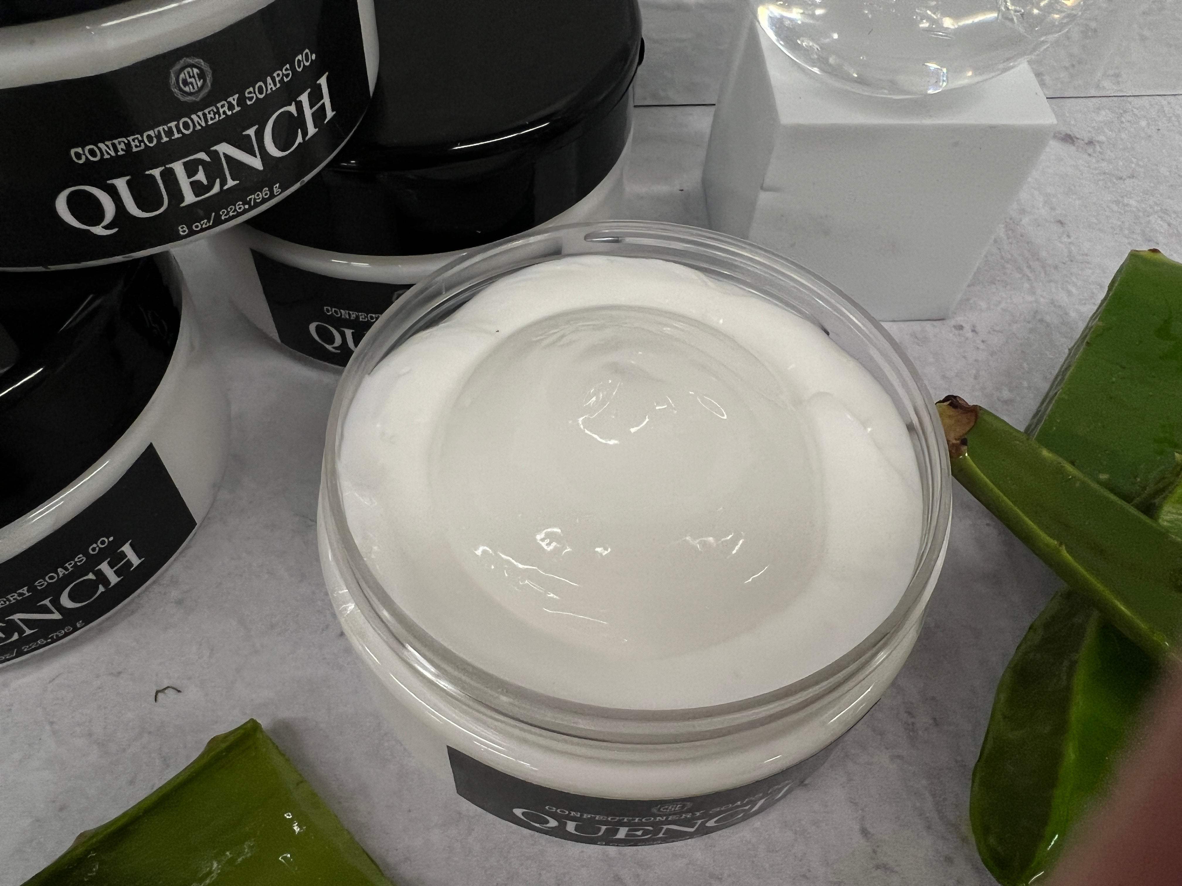 a zoomed in picture of the open quench jar, so you are able to see the aloe gel center surrounded by the lotion. stacked quench jars and aloe plant pieces are slightly visible as they are part of the listing's decorations.