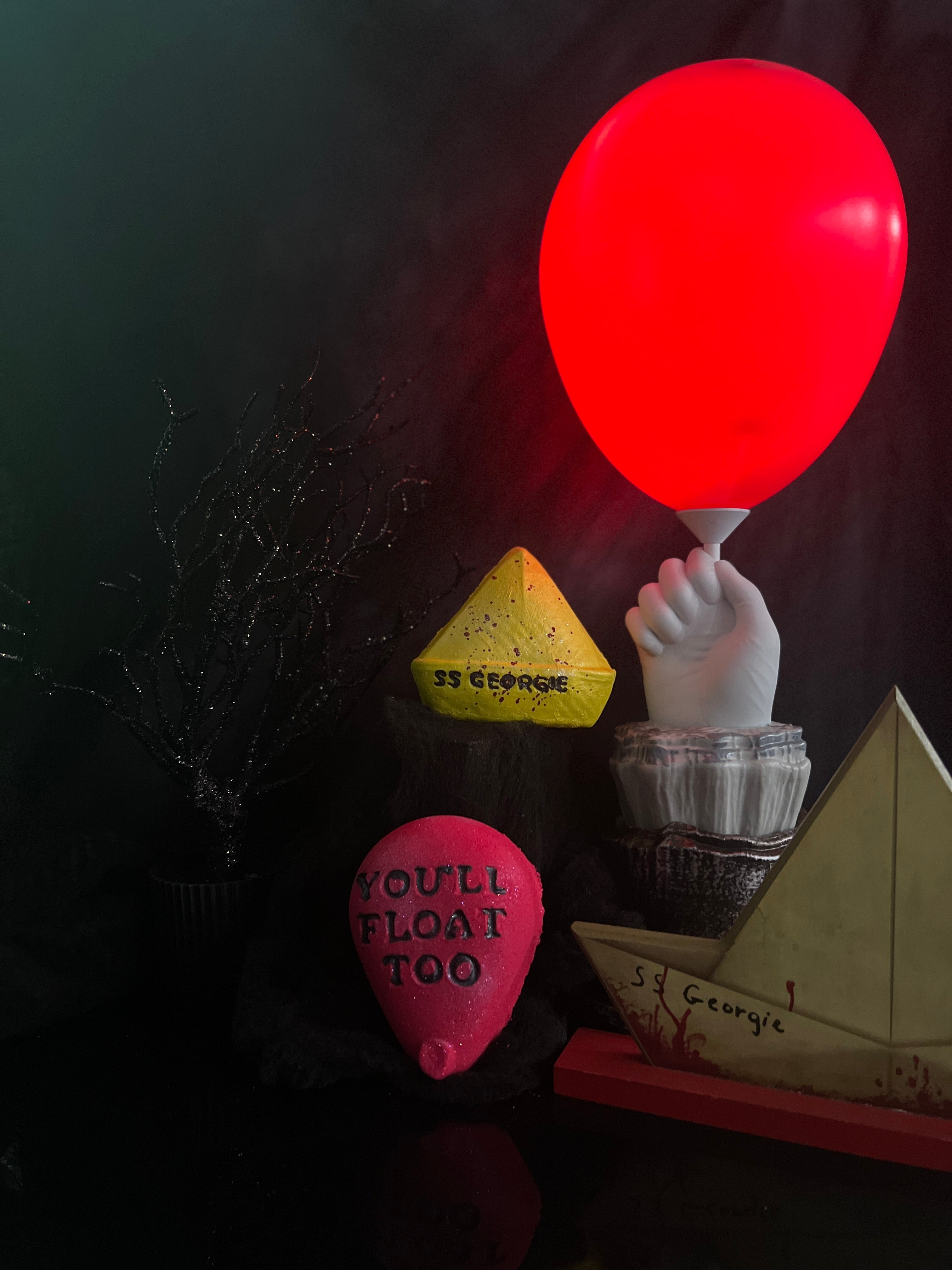 one red  balloon bath bomb and one yellow boat shaped bath bomb with image of red balloon and boat as props in the background